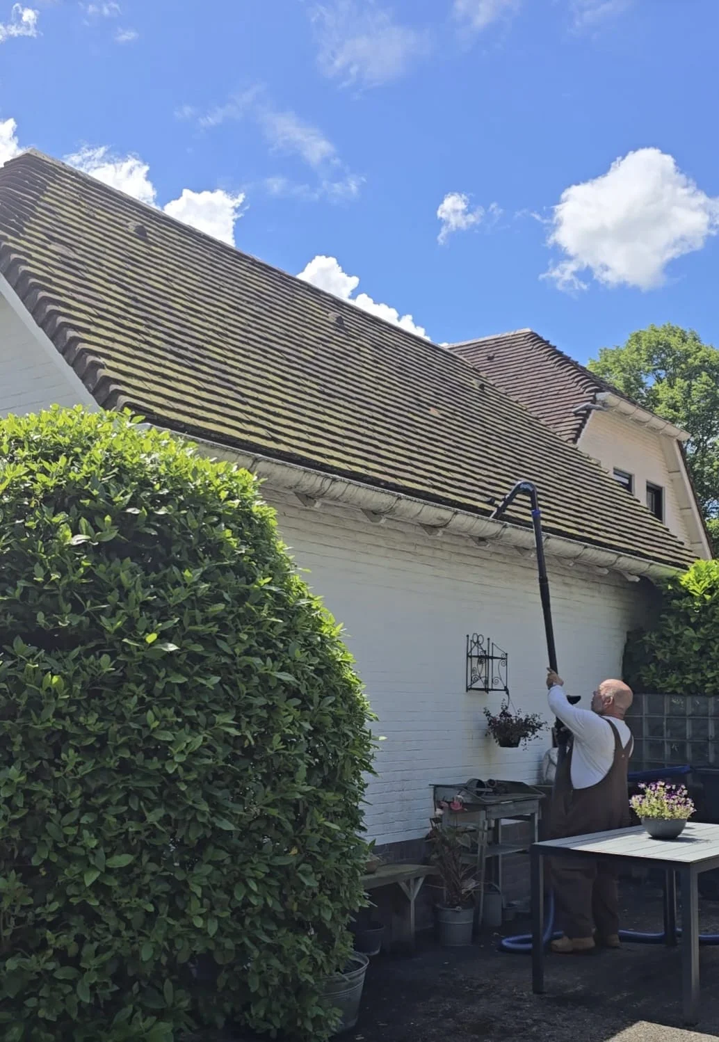 Peter reinigt de dakgoot van een witte woning