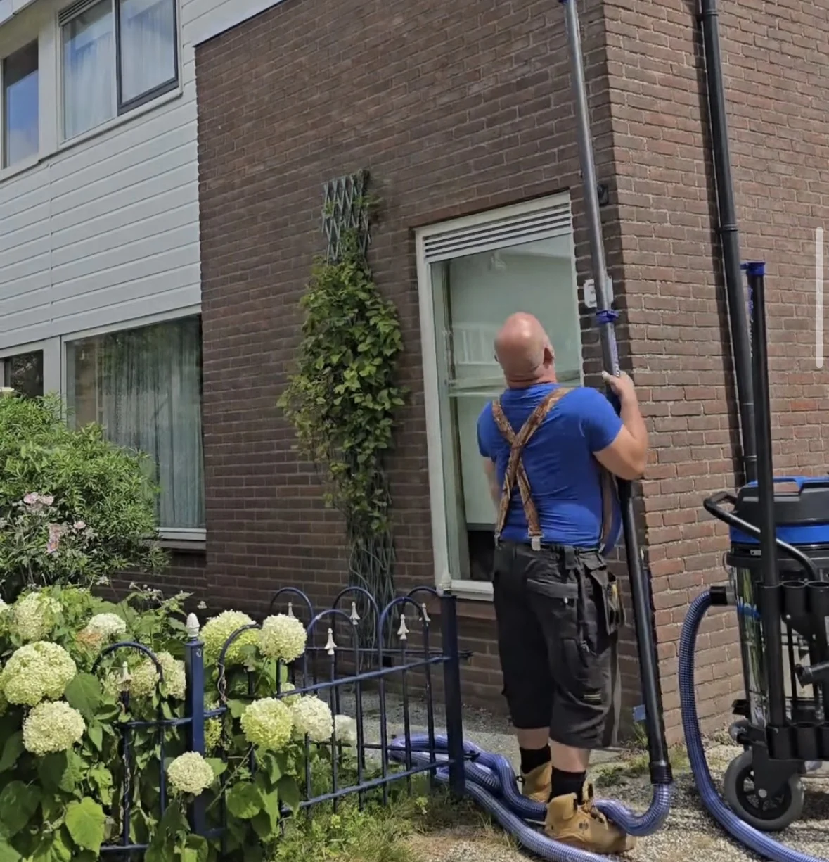 Dakgootspecialist reinigt de dakgoot van een woning met een lange zuigbuis